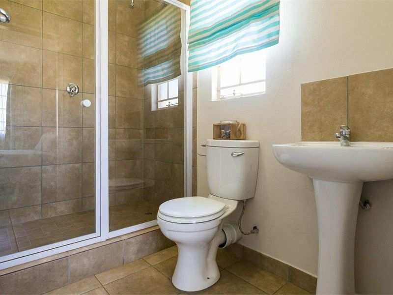 A functional bathroom featuring a pedestal basin, toilet, and a tiled shower enclosure with a glass door.