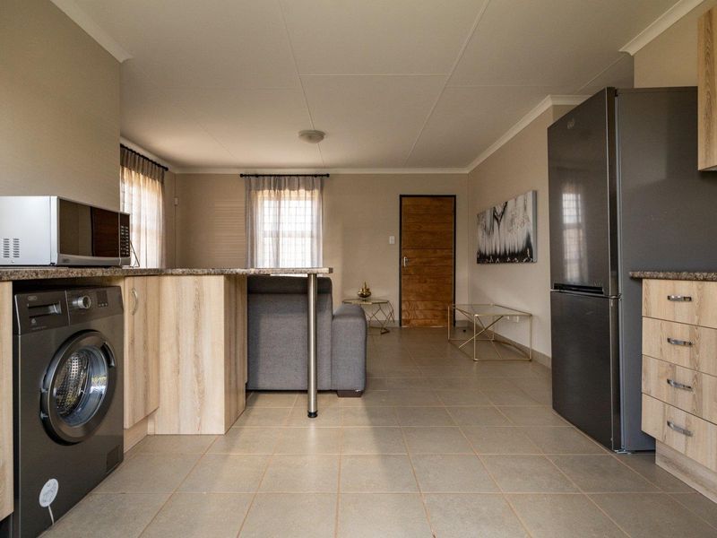 Open-plan living area featuring a functional kitchen with light wood cabinetry, tiled floors, and integrated appliance connections, flowing into the main living space.