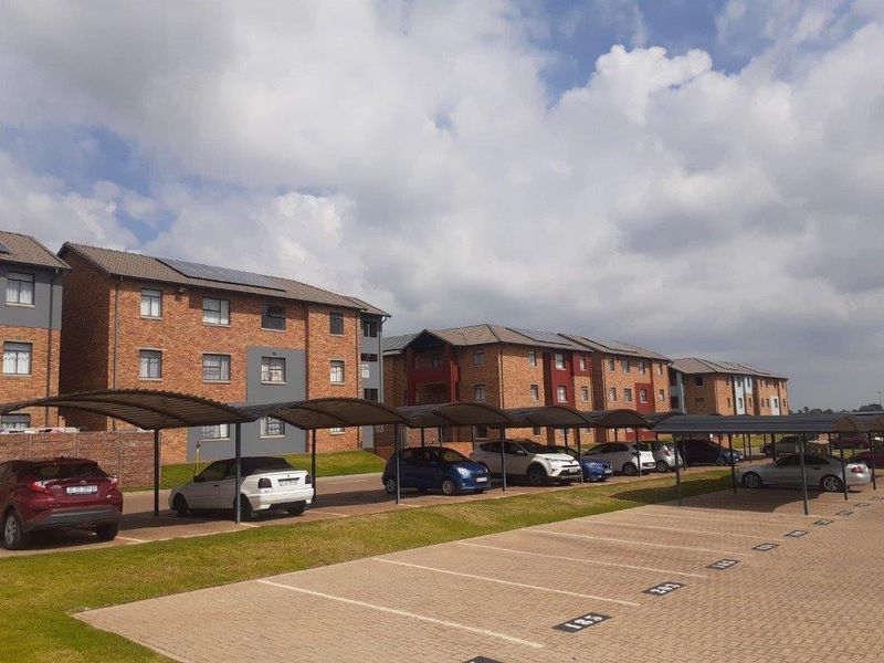 Exterior view of an apartment complex featuring brick buildings, covered parking bays, and solar panel installations on the roofs.