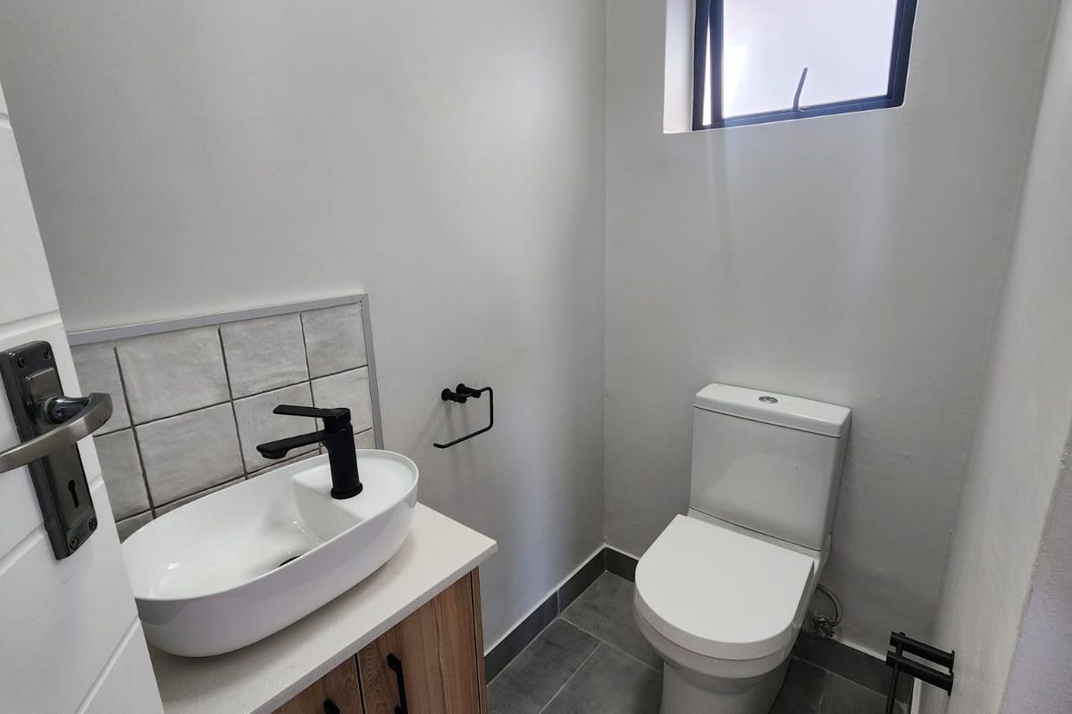 A modern, compact guest bathroom featuring a contemporary vessel sink, black fixtures, and neutral tiled flooring.