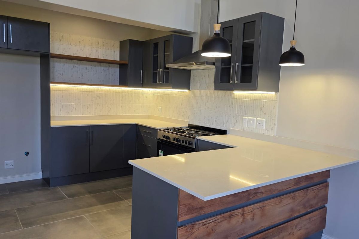 Modern kitchen featuring dark cabinetry, stone countertops, gas stove, extractor fan, and stylish pendant lighting with a clean, contemporary finish.