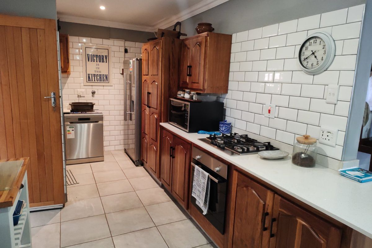A functional kitchen featuring wooden cabinetry, stone countertops, a gas hob, built-in oven, and a classic white subway tile backsplash.