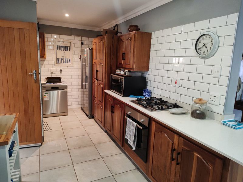 A functional kitchen featuring wooden cabinetry, stone countertops, a gas hob, built-in oven, and a classic white subway tile backsplash.