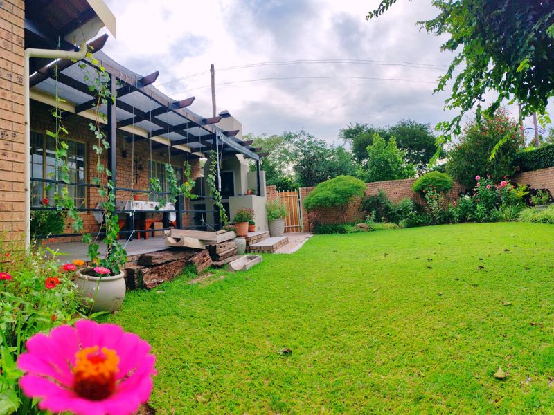 A well-maintained rear garden featuring a covered patio with a built-in braai, brick facade, and established lawn area.