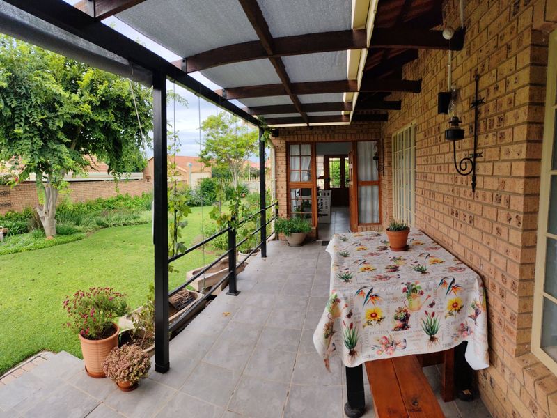 A covered outdoor patio featuring exposed brick walls, tiled flooring, and a timber pergola structure overlooking a well-maintained garden.