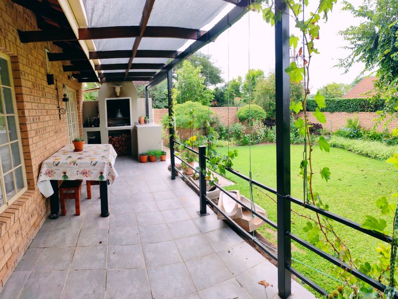 A covered patio featuring a built-in braai, tiled flooring, and a metal pergola, overlooking a well-maintained garden.