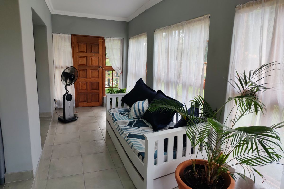 A bright living area featuring tiled flooring, a solid timber entrance door, and large windows allowing for ample natural light.