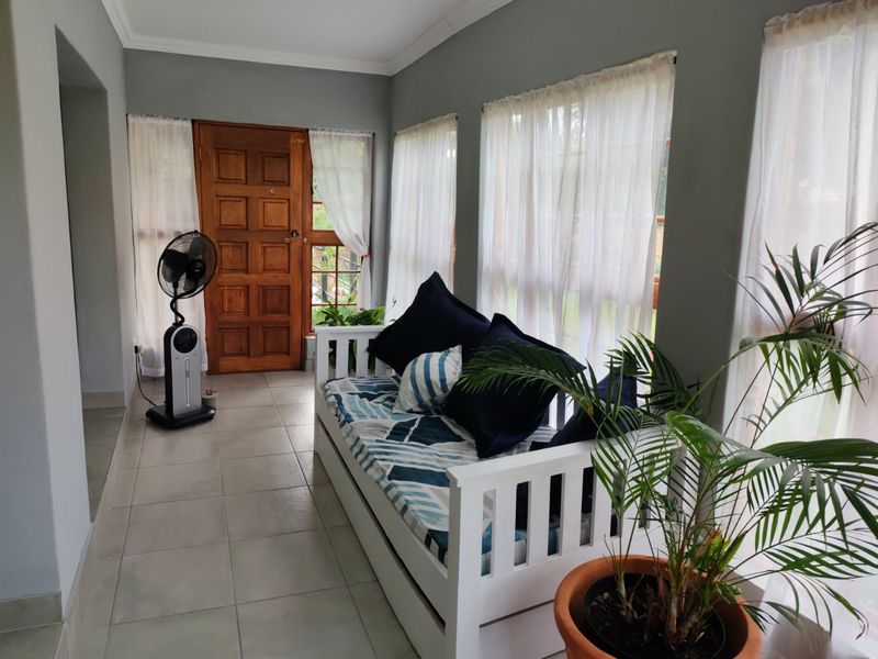 A bright living area featuring tiled flooring, a solid timber entrance door, and large windows allowing for ample natural light.