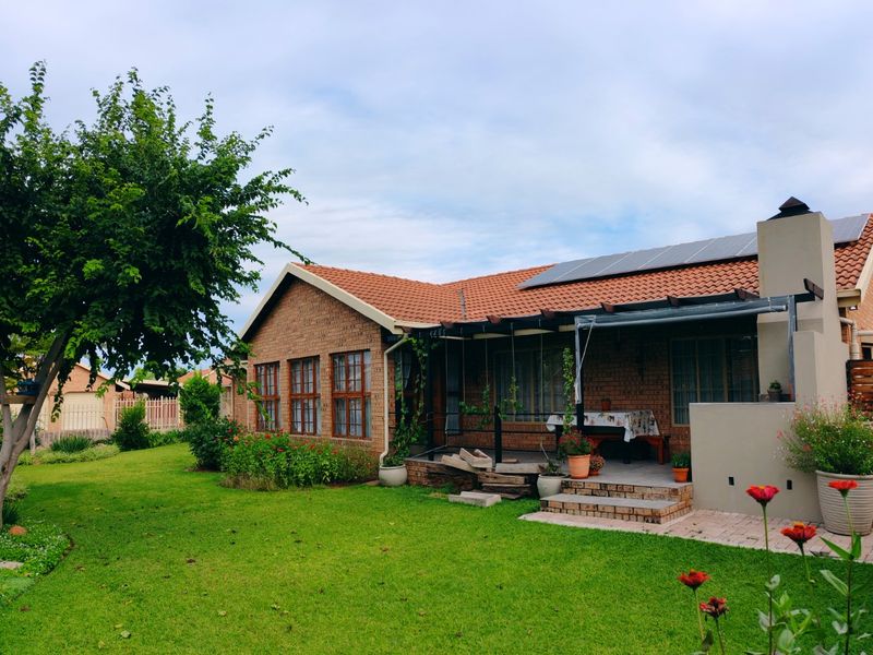 Rear view of a brick house featuring a covered patio, outdoor fireplace, solar panels, and a well-maintained garden.