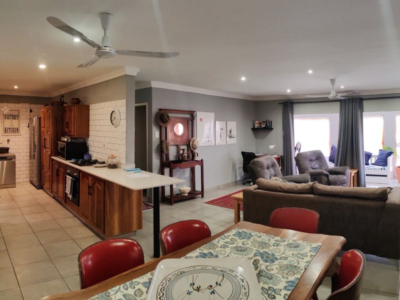 Spacious open-plan living area featuring a functional kitchen with wooden cabinetry, tiled floors, recessed lighting, and seamless flow to the outdoor patio area.