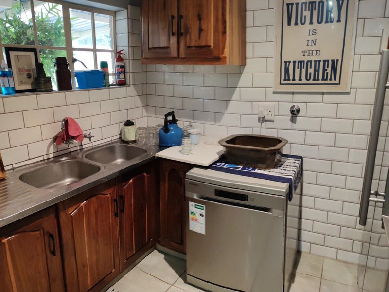 A functional scullery area featuring wooden cabinetry, a double stainless steel sink, and a classic white subway tile backsplash.