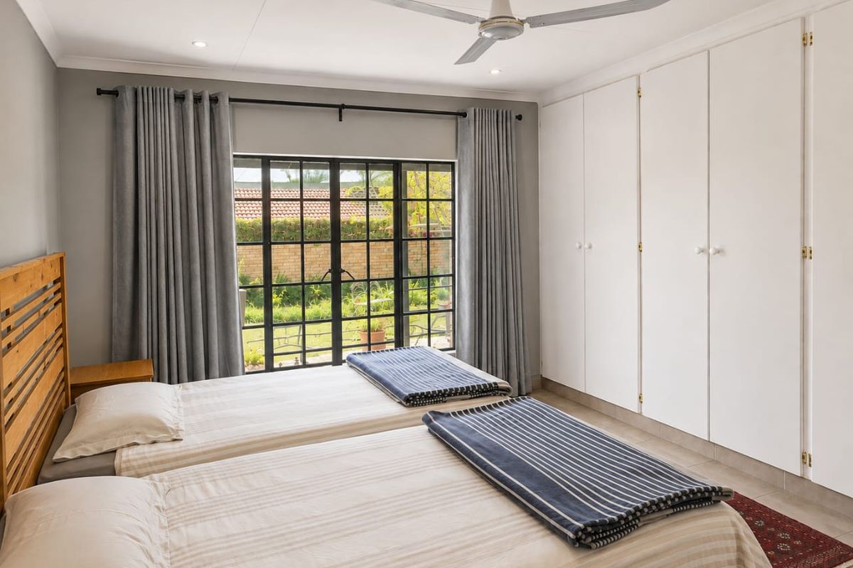 A well-maintained bedroom featuring built-in cupboards, a ceiling fan, and french doors providing direct access to the garden.