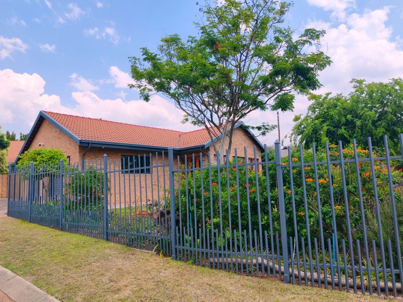 A well-maintained face brick house featuring a tiled roof, secured by steel palisade fencing and surrounded by established garden greenery.