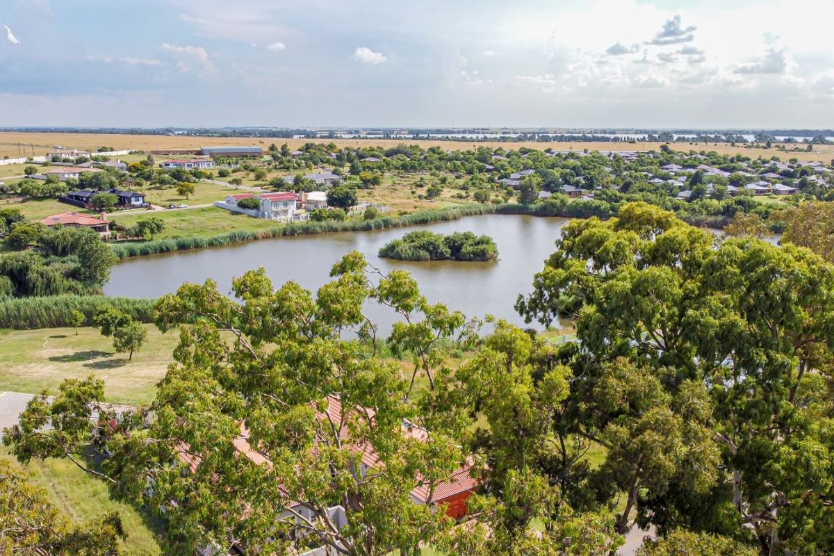 An elevated aerial view showcasing the surrounding landscape, featuring a scenic lake and established greenery within the estate.