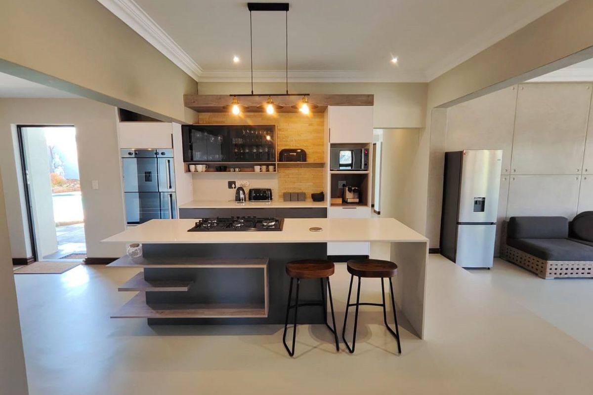 Modern open-plan kitchen featuring a central island with gas hob, sleek cabinetry, built-in appliances, and contemporary pendant lighting.