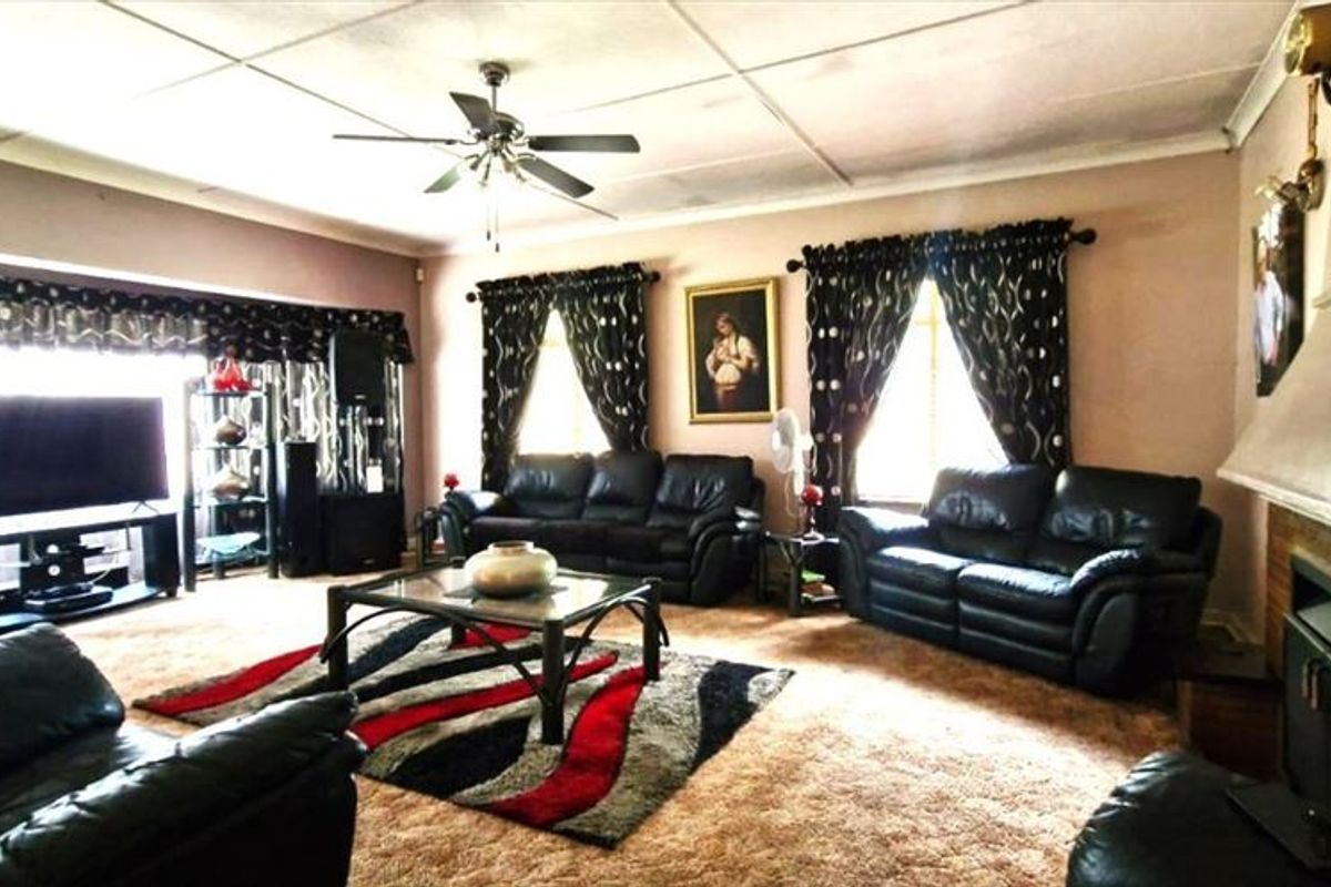 Spacious living room featuring a brick fireplace, ceiling fan, and large windows, offering a traditional layout with potential for modernization.
