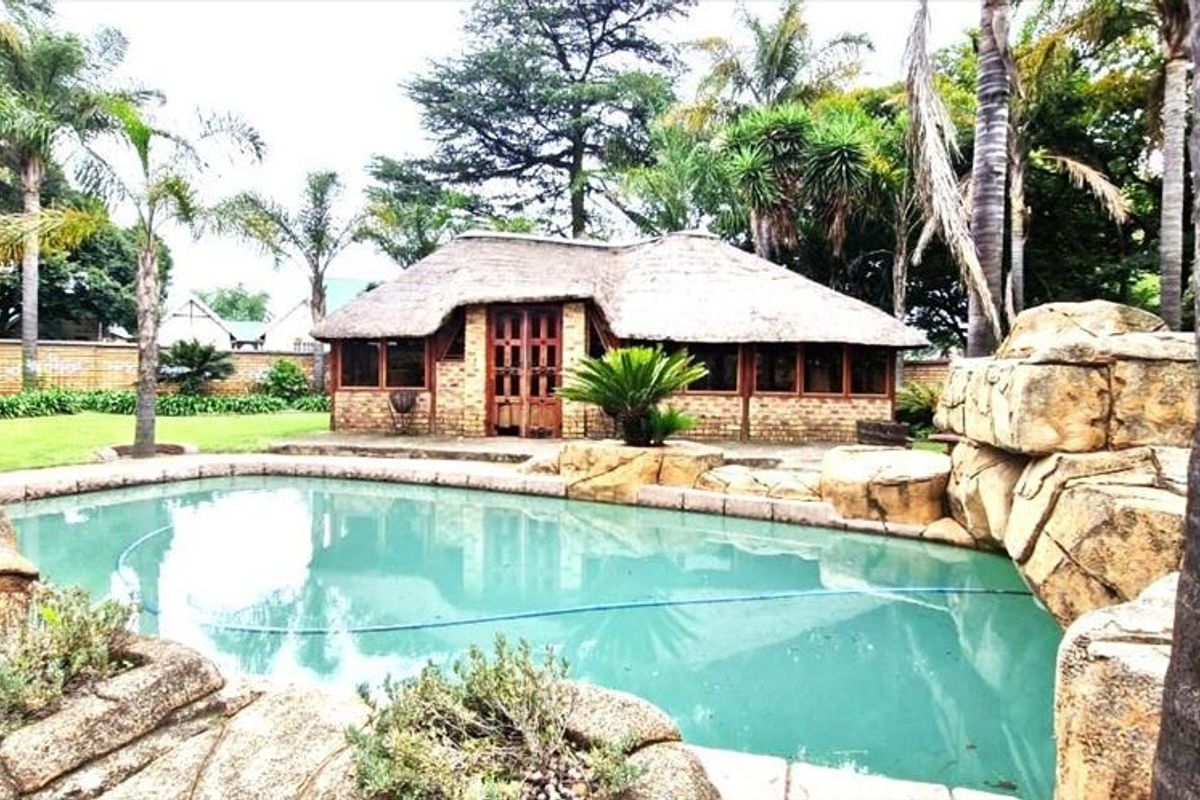 A backyard pool area featuring a rock-style swimming pool and a thatched-roof entertainment structure set within a landscaped garden.