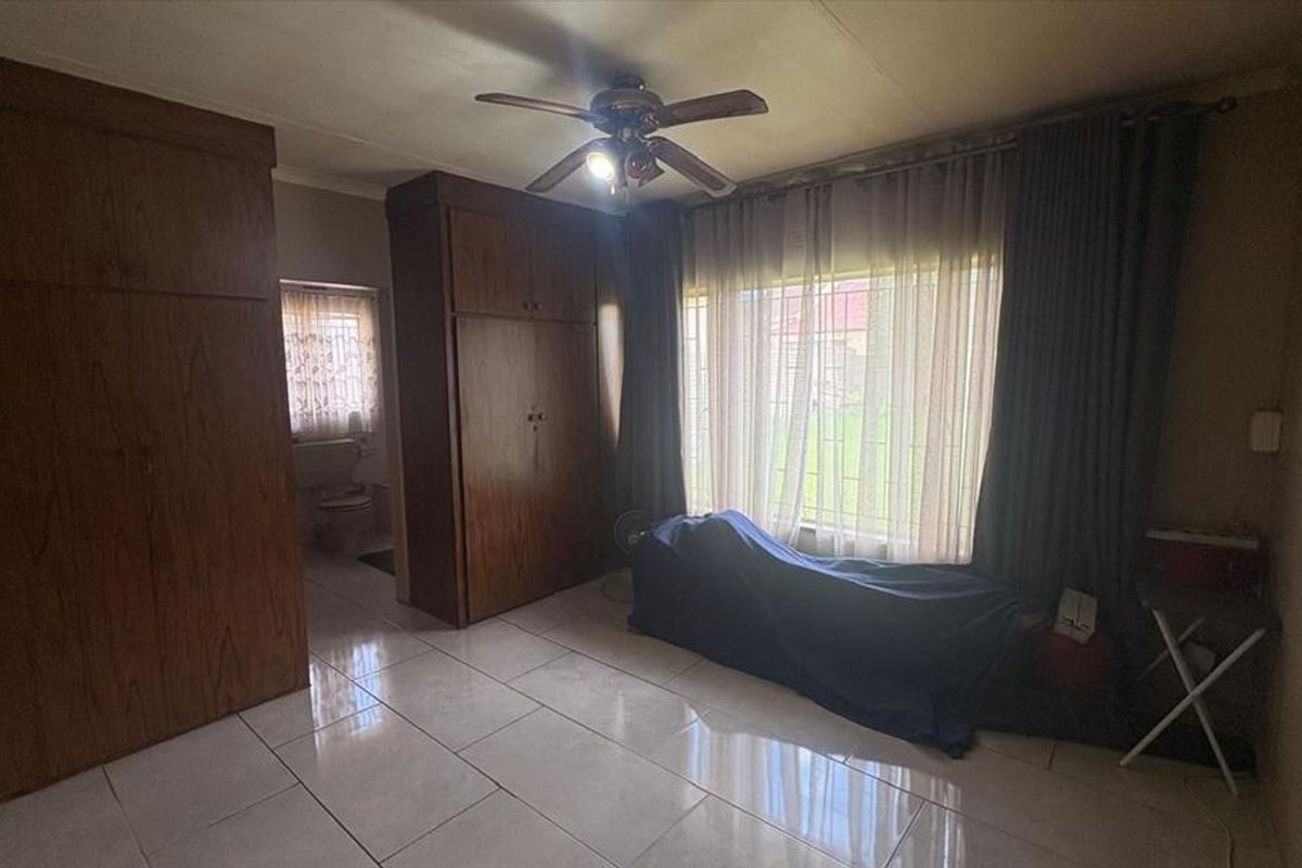 Bedroom featuring built-in wooden cupboards, tiled flooring, and a ceiling fan, with direct access to an en-suite bathroom area.