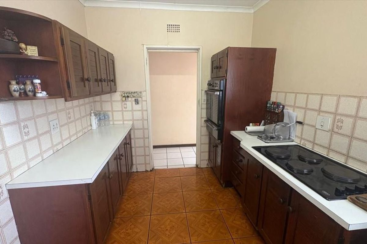 A dated kitchen featuring dark wood cabinetry, laminate countertops, ceramic wall tiling, and built-in cooking appliances, offering potential for a modern renovation.