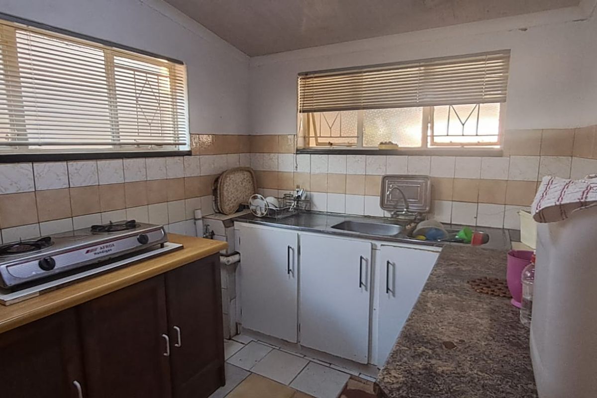 A functional kitchen featuring built-in cabinetry, a stainless steel sink, gas hob, and tiled splashbacks, requiring cosmetic updates to modernize the space.