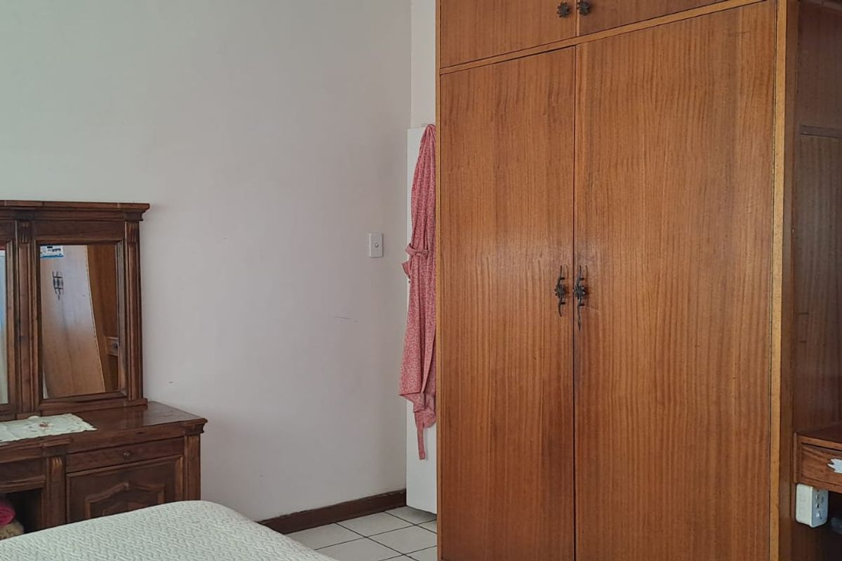 A bedroom featuring tiled flooring and a large built-in wooden wardrobe, offering functional storage space.