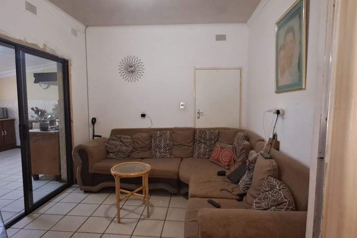 A living room featuring tiled flooring and a sliding glass door leading to the kitchen area, with visible signs of wear on the wall finishes.