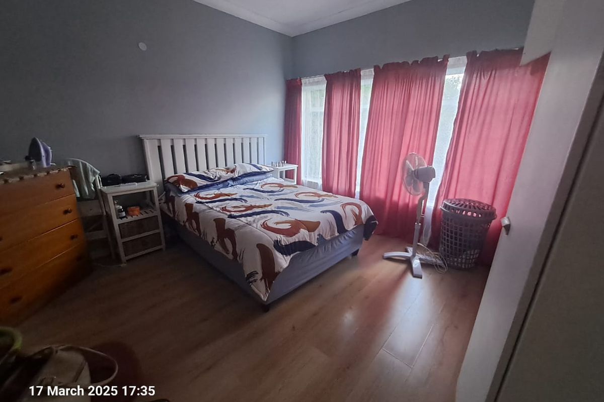 A bedroom featuring laminate flooring and neutral wall finishes, providing a functional space with natural light through large windows.