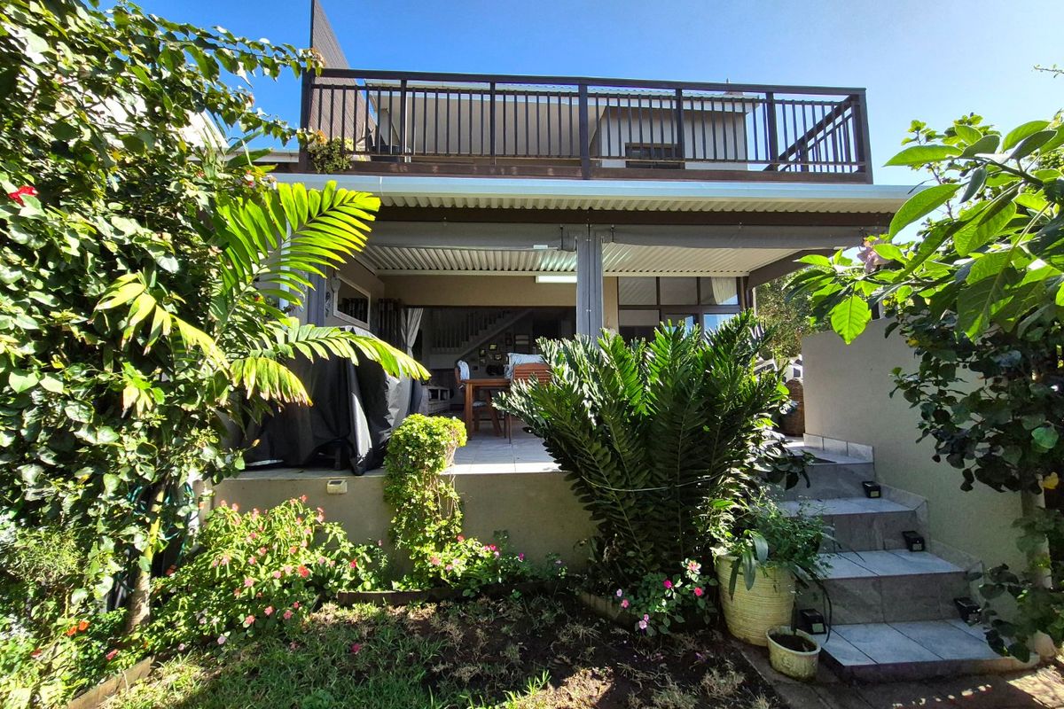 Rear view of the townhouse featuring a covered ground-floor patio, an upper-level balcony with railing, and landscaped garden access via tiled stairs.