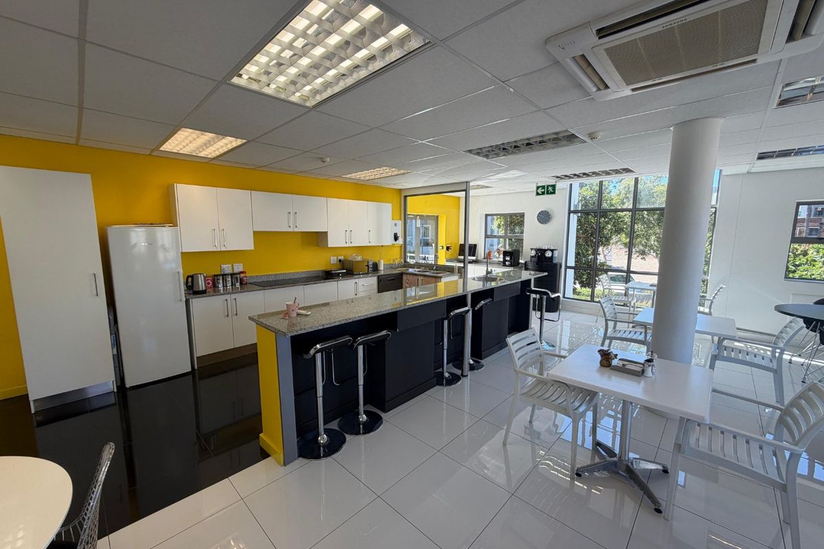 A bright, open-plan commercial kitchen and break area featuring a granite-topped breakfast bar, modern cabinetry, and large windows providing ample natural light.