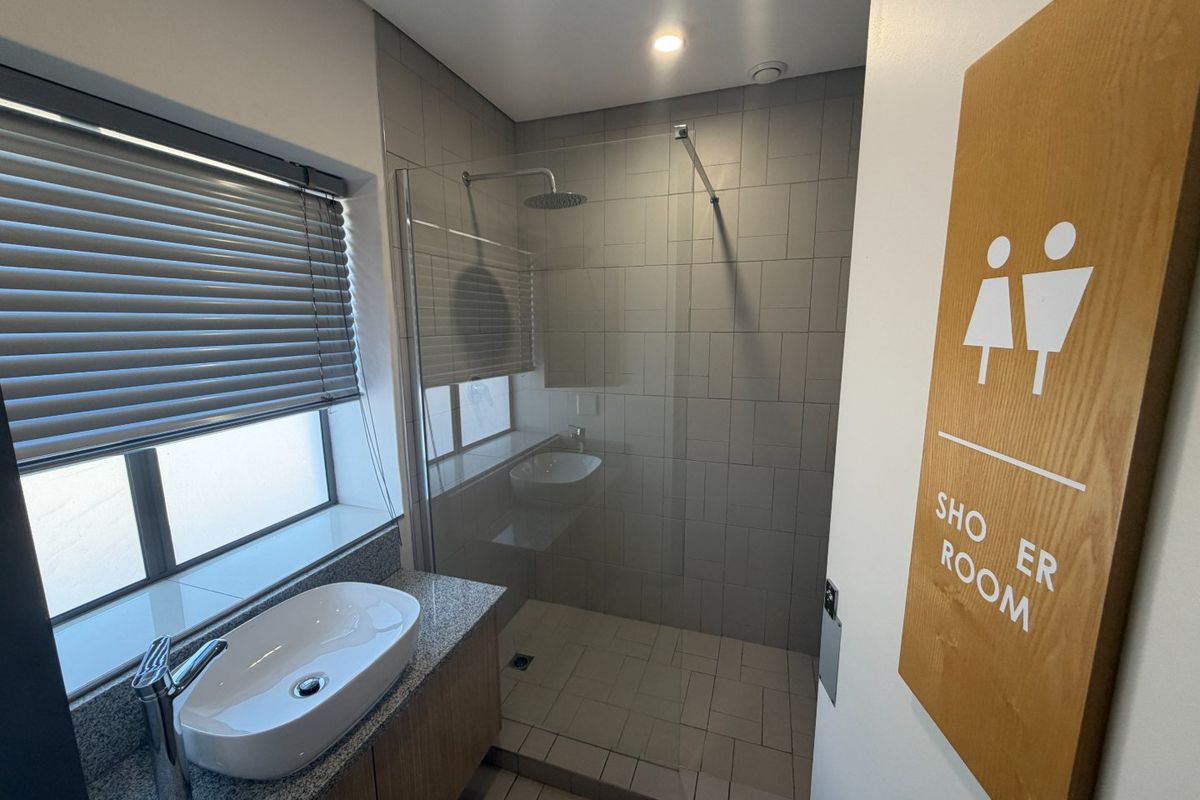 Modern commercial shower room featuring a glass-enclosed walk-in shower, contemporary vanity with stone countertop, and neutral tiled finishes.