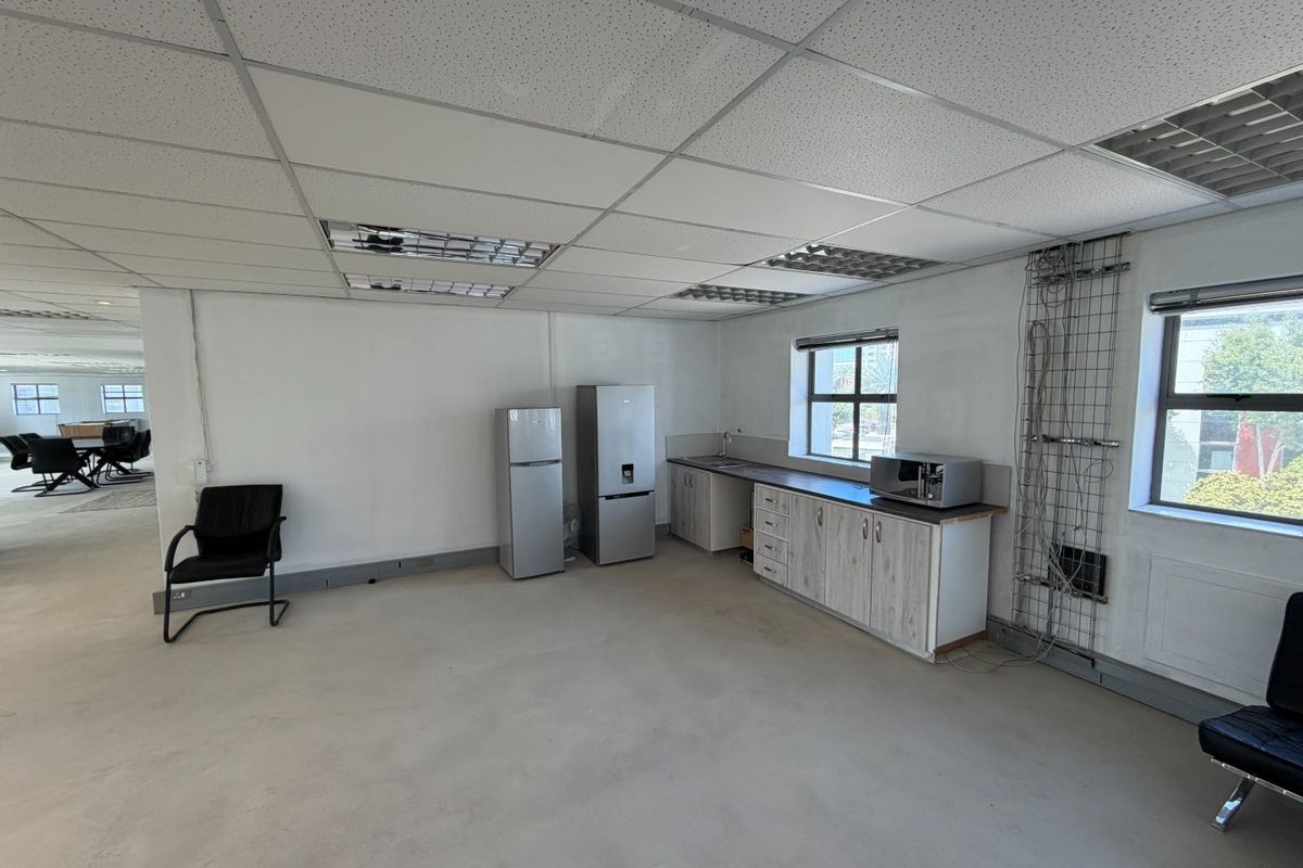 A functional commercial kitchenette area featuring built-in cabinetry, a sink, and integrated workspace within an open-plan office environment.