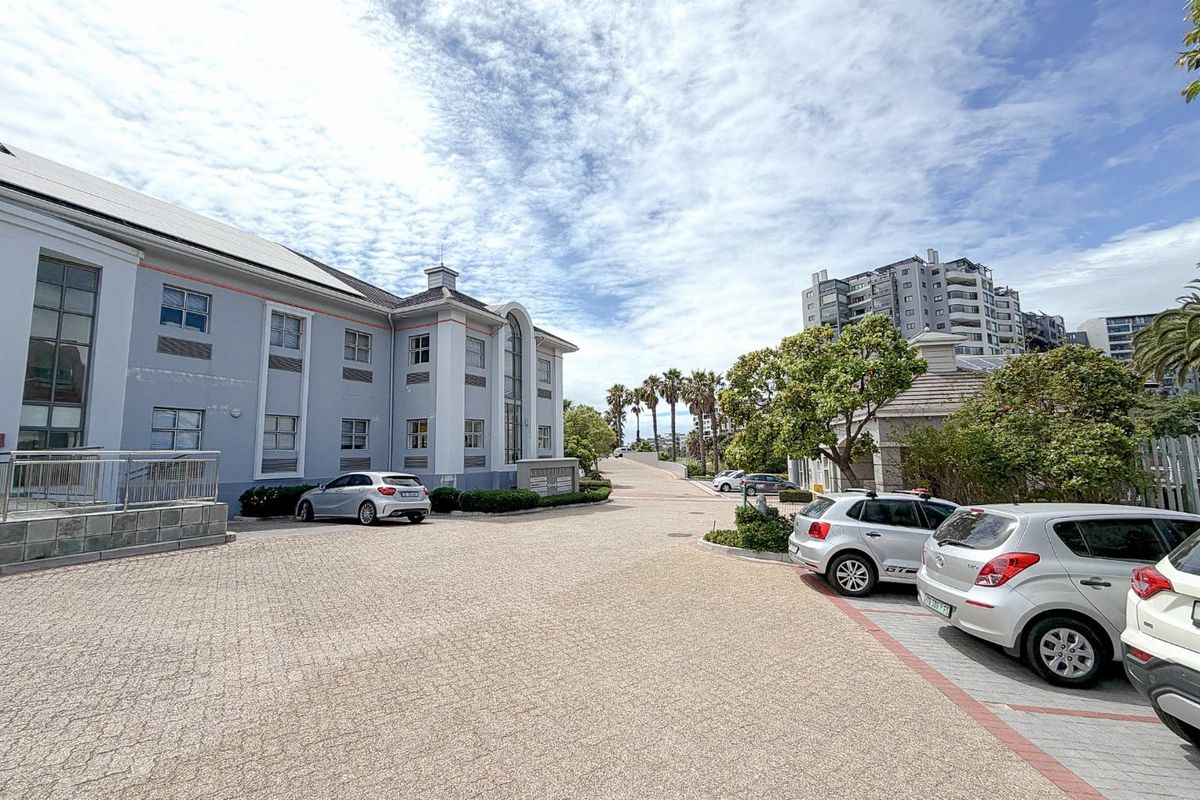 Exterior view of a commercial office building featuring a paved driveway, landscaped garden areas, and multi-story facade with large windows.