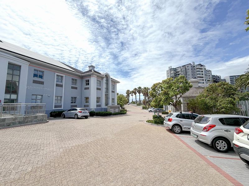 Exterior view of a commercial office building featuring a paved driveway, landscaped garden areas, and multi-story facade with large windows.