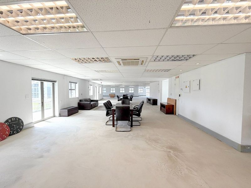 Spacious open-plan commercial office area featuring a suspended ceiling with recessed lighting, ducted air conditioning, and large sliding glass doors providing natural light.