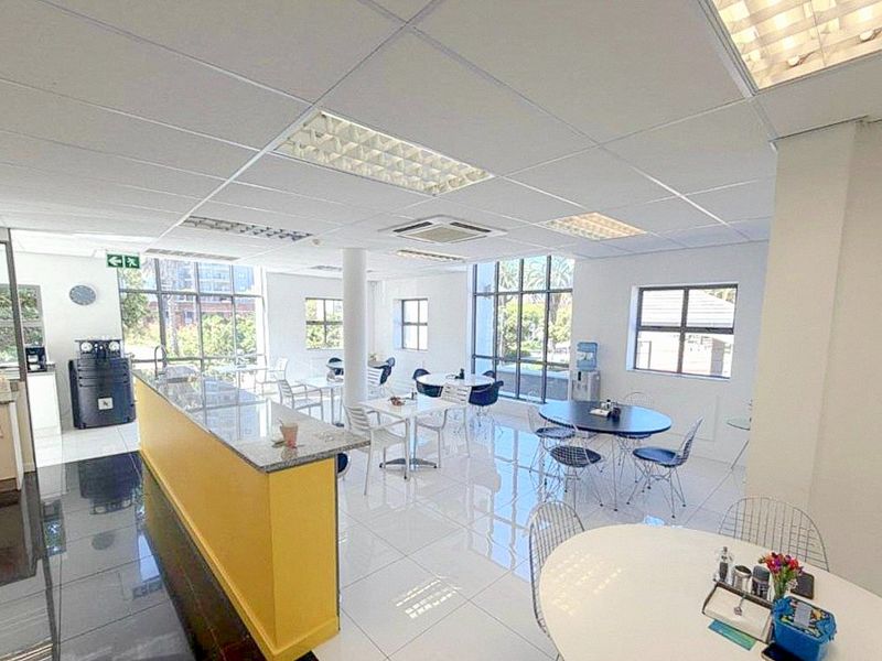 Bright open-plan commercial office space featuring tiled flooring, suspended ceilings with recessed lighting, and large windows providing ample natural light.