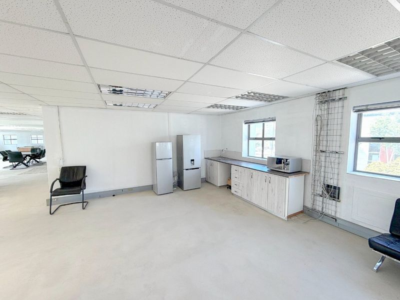 A functional commercial kitchenette area featuring built-in cabinetry, a stainless steel sink, and suspended ceiling tiles, suitable for office staff use.