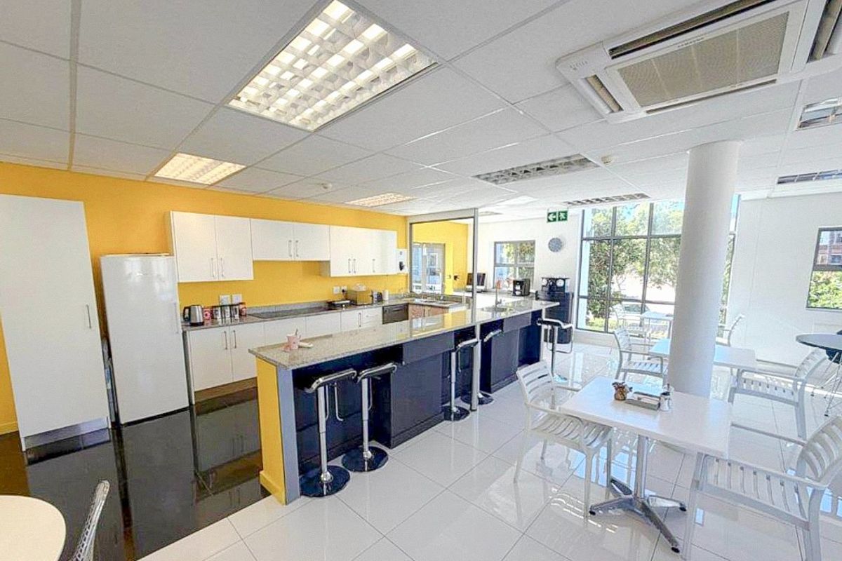 A bright commercial kitchen and break area featuring white cabinetry, granite countertops, tiled flooring, and large windows providing ample natural light.