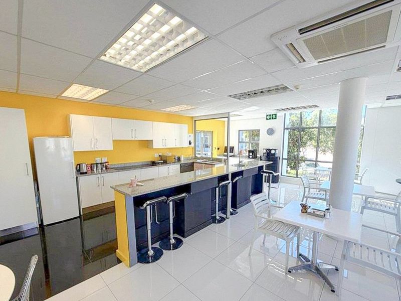 A bright commercial kitchen and break area featuring white cabinetry, granite countertops, tiled flooring, and large windows providing ample natural light.