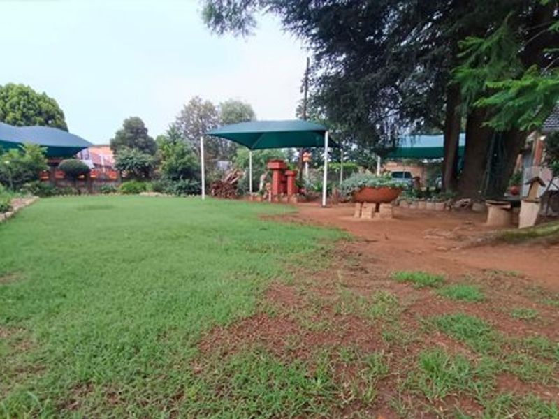 A spacious outdoor garden area featuring mature trees, a green shade sail structure, and a mix of lawn and natural ground cover.