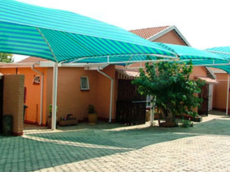 Exterior view of a commercial property featuring a paved driveway and large turquoise shade sail structures providing covered parking.