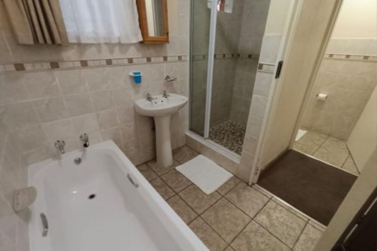 A functional bathroom featuring a pedestal washbasin, a built-in bathtub, and a separate shower enclosure with neutral ceramic wall and floor tiles.