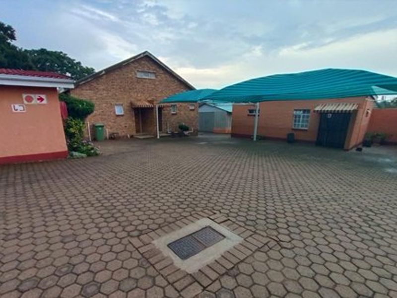 A paved commercial courtyard area featuring a shade cloth carport, brick building facades, and secure access points.