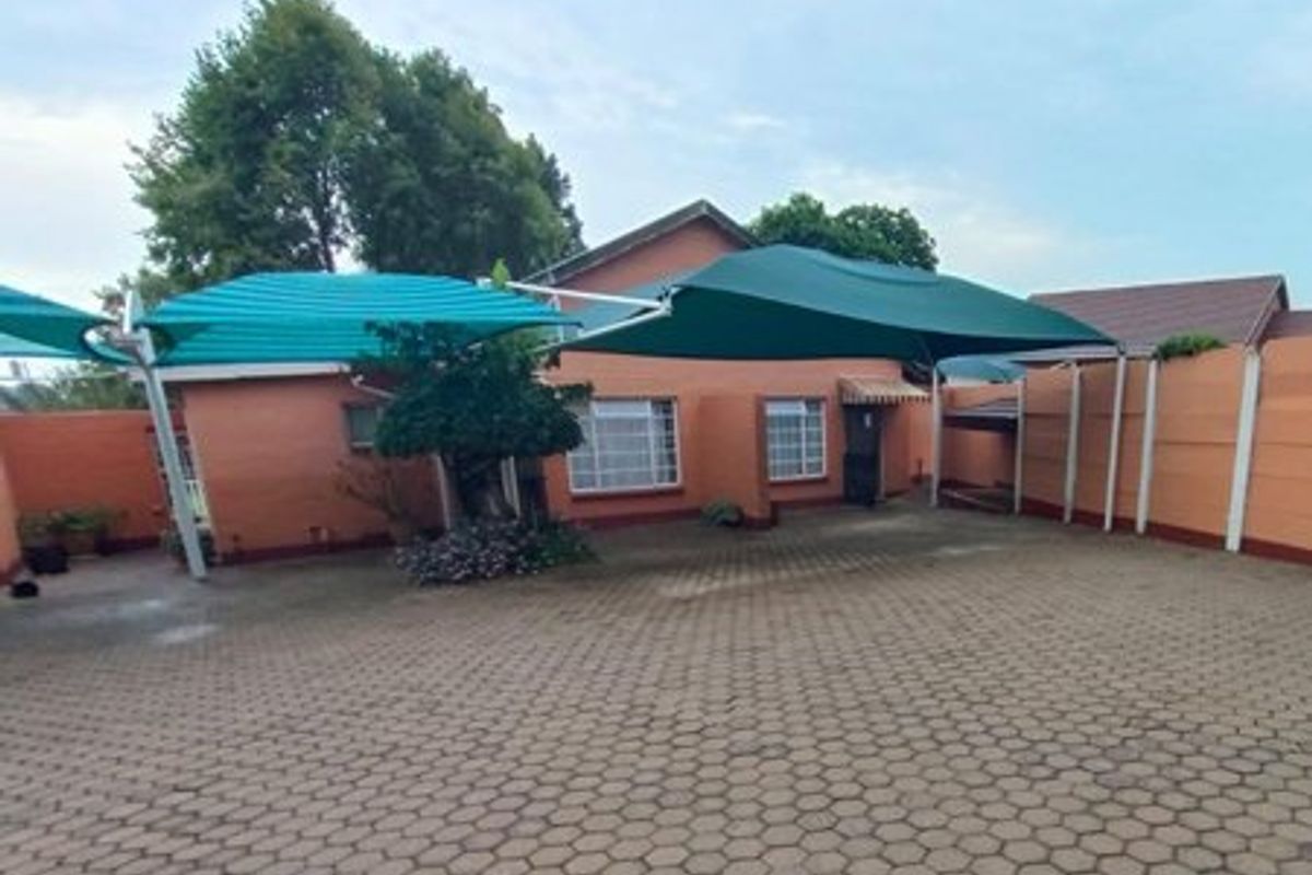 Rear exterior view of the property featuring a large paved courtyard, shade cloth carports, and perimeter boundary walls.