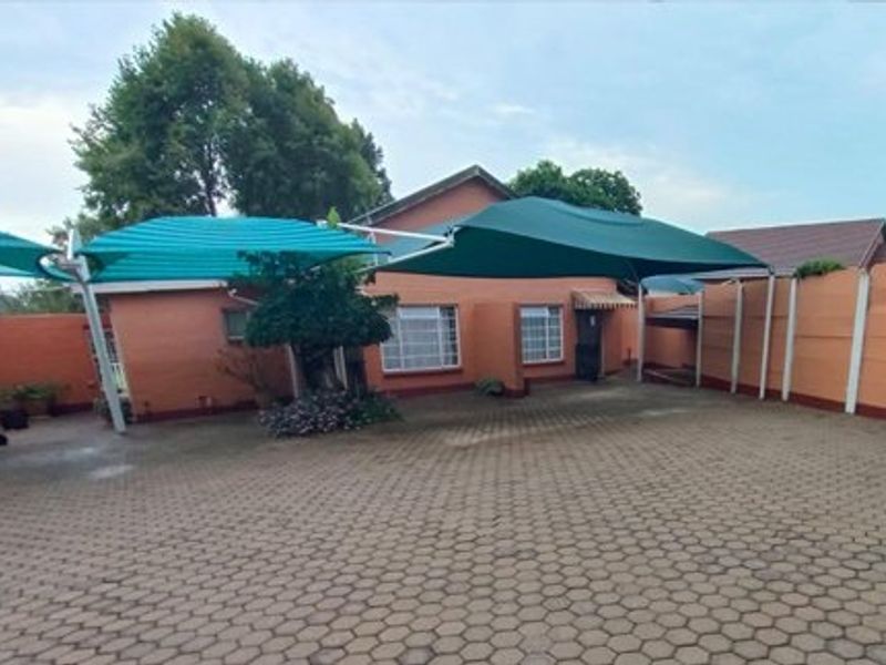 Rear exterior view of the property featuring a large paved courtyard, shade cloth carports, and perimeter boundary walls.