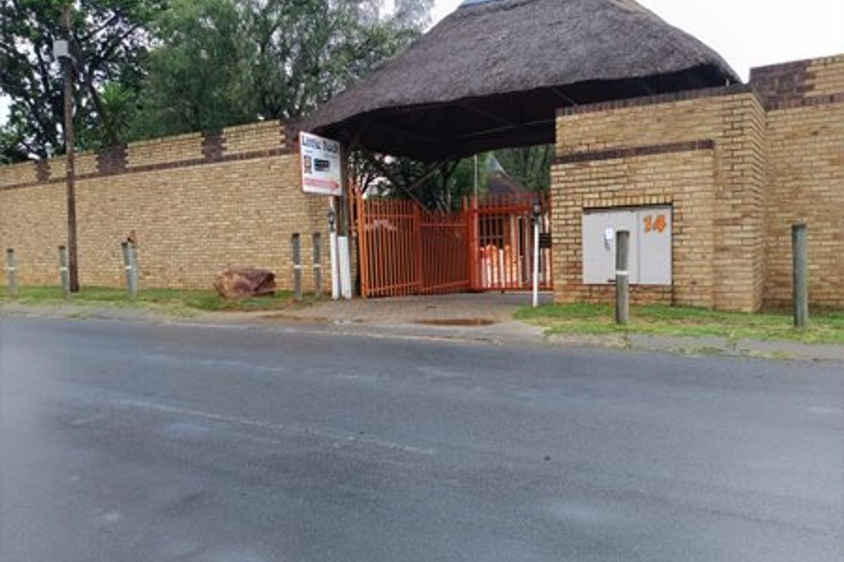Front street view of a commercial property entrance featuring a brick boundary wall and a distinctive thatched roof gate structure.