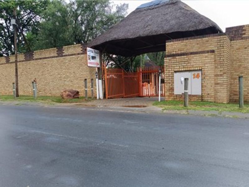 Front street view of a commercial property entrance featuring a brick boundary wall and a distinctive thatched roof gate structure.