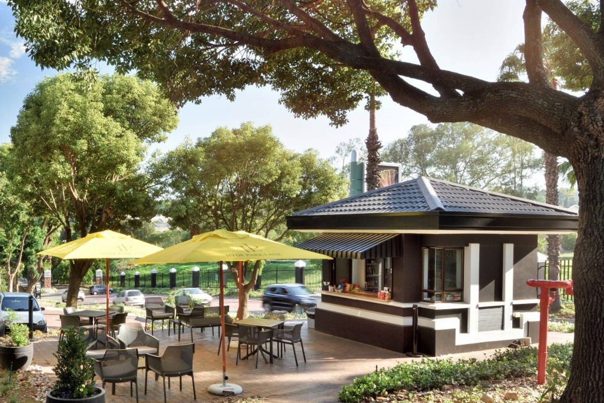 A well-maintained outdoor patio area featuring a permanent kiosk structure, paved flooring, and mature trees, providing an inviting space for commercial use.