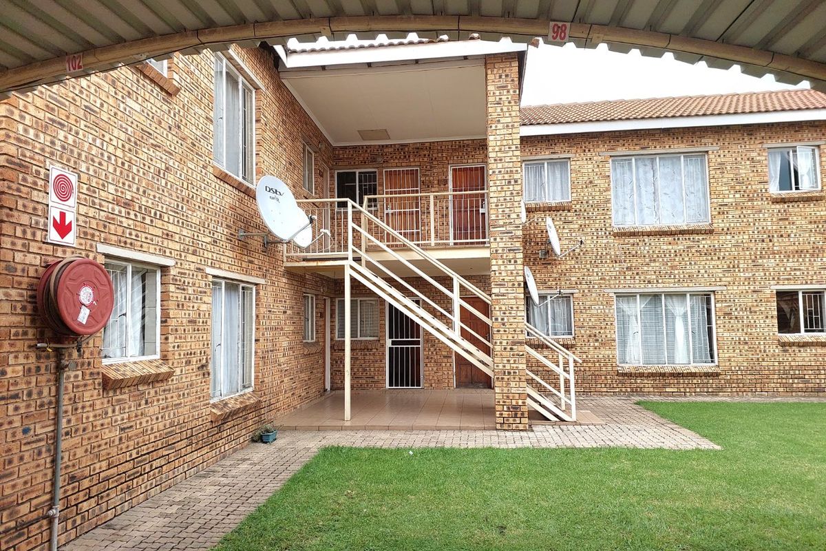 Exterior view of a face brick apartment complex featuring a central metal staircase, paved walkways, and a shared lawn area.