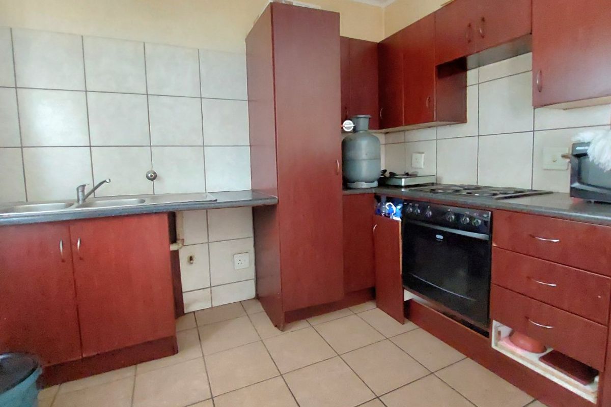 A functional kitchen featuring dark wood-look cabinetry, a built-in oven with gas hob, tiled splashbacks, and tiled flooring, requiring some cosmetic updates.
