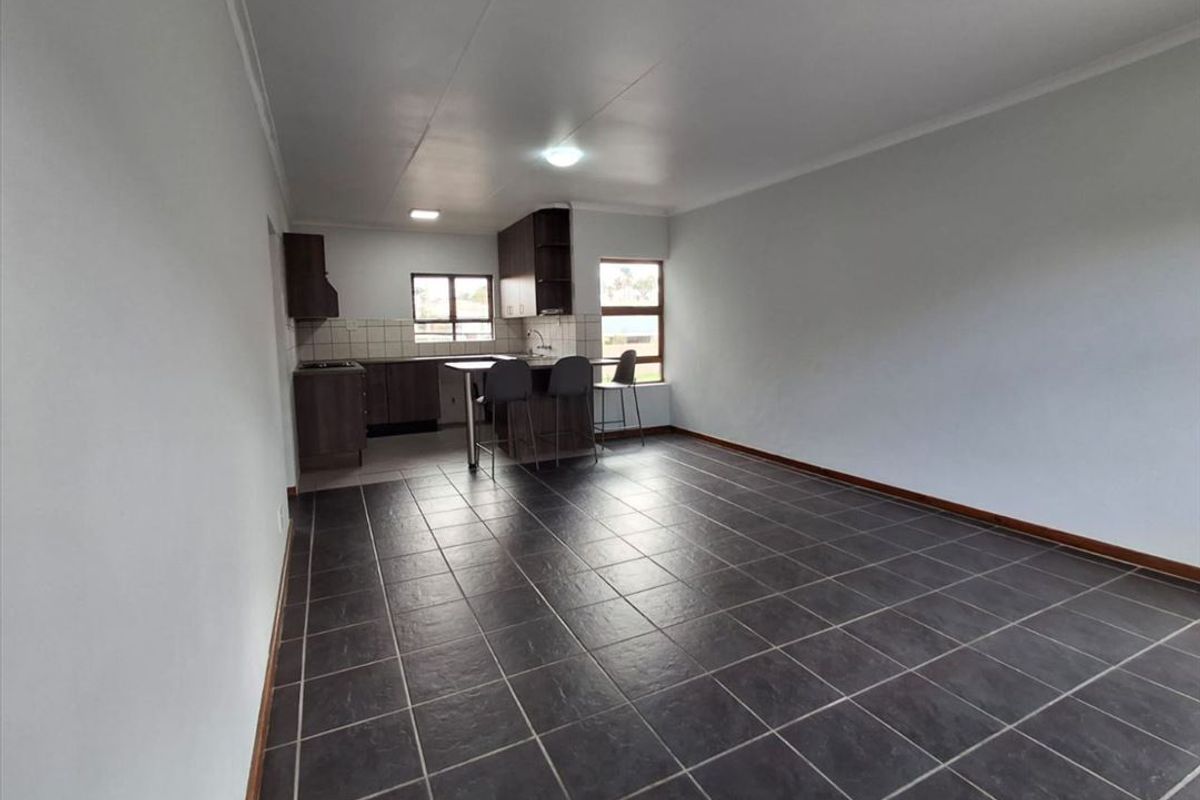 Open-plan living and kitchen area featuring dark tiled flooring, built-in cabinetry, and a breakfast counter in a neutral, well-lit space.